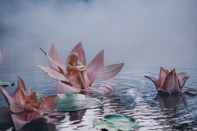 Happy young little blonde woman sits in huge pink flower lotus on water. Fantasy artistic photo. Beautiful girl in a fairy tale lake. Girl Thumbelina. Image Goddess of nature in blue mystic river fog (foto: Shutterstock Shutterstock)