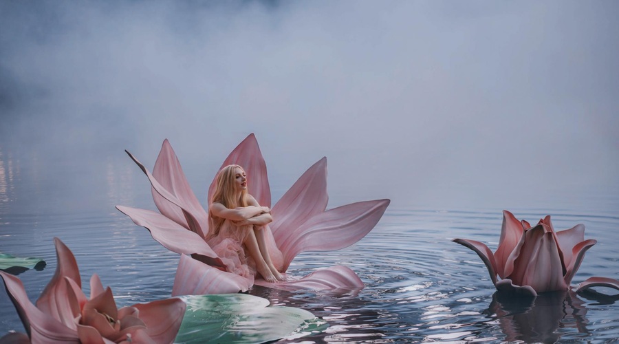 Happy young little blonde woman sits in huge pink flower lotus on water. Fantasy artistic photo. Beautiful girl in a fairy tale lake. Girl Thumbelina. Image Goddess of nature in blue mystic river fog (foto: Shutterstock Shutterstock)